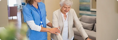 Caregiver assisting an older woman as she carefully walks, providing support to prevent falls.