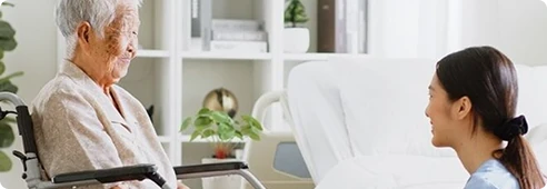 Caregiver speaking with an elderly woman in a wheelchair in a calm, supportive home setting.